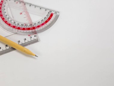 Yukarıdan aşağıya doğru çekimde, beyaz bir yüzeyde açıölçer, cetvel ve kalem ustalıkla yerleştirilmiş. Kompozisyon, matematik ve geometride kullanılan düzen ve hassasiyet duygusunu ileten araçları vurgular. Temiz plastik enstrümanlar ve s