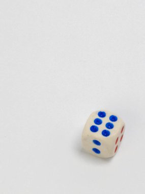 Sade beyaz bir arkaplanda duran tek bir zarın yakın plan çekimi, basitliği ve odaklanmayı vurguluyor. Zarlar krem renginde, mavi noktalar ve kırmızı noktalar ile 1-6 rakamlarını gösteriyor. Kompozisyon temiz ve minimal, objeyi vurguluyor. Şey... 