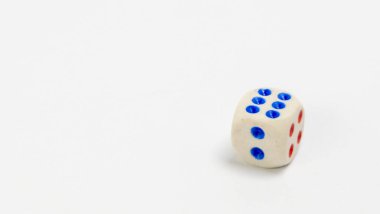 Beyaz bir yüzeyde tek bir atışın yakın çekimi ölür. Zarlar beyaz, mavi ve kırmızı noktalar var. 6 ve 4 rakamlarını gösteriyor. Görüntü, zarın detaylarını vurgulayan temiz bir arkaplan ile iyi aydınlatılmış. Kompozisyon basit, alt bölüme izin veriyor.