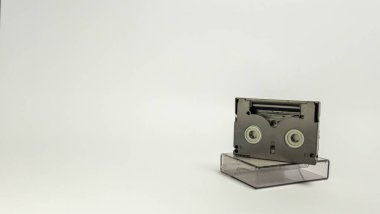 Şeffaf plastik kılıfının üzerinde duran bir MiniDV kasetinin yakın çekim çekimi. Kaset, metin veya diğer tasarım unsurları için geniş negatif alanı olan düz beyaz bir arkaplana odaklanmış durumda. T 'nin dokusunu ve tasarımını vurgular