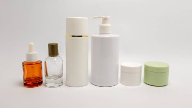 Şişeler, kavanozlar ve şeker kutuları da dahil olmak üzere çeşitli cilt bakım ürünlerinin bir koleksiyonu, düz beyaz arka planda bir sıraya dizilmiştir. Ürünler tarafsız renklerde ve kehribar camlı. Güzellik, kozmetik ve cilt konseptleri için uygun. Th