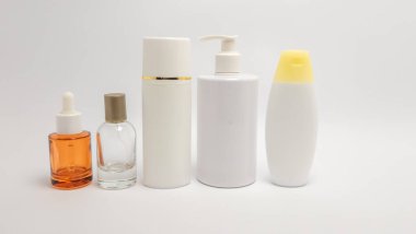 Beyaz arka planda çeşitli kozmetik şişeler ve konteynırların yer aldığı bir stüdyo resmi. Resimde bir damlatıcı şişesi, bir sprey şişesi, uzun bir silindirik şişe, bir pompa şişesi ve bir şampuan şişesi var. Şişeler farklı şekillerde. 