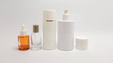 Cilt bakım ürünleri şişeleri ve kavanozlar beyaz arka planda sıralanır. Resimde bir serum şişesi, bir sprey şişesi, uzun bir silindirik şişe, bir pompa şişesi ve küçük bir kavanoz var, hepsi de tarafsız tonlarda. Kompozisyon I