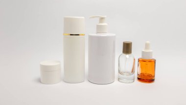 Bu resim, beyaz bir zemin üzerine kurulmuş çeşitli şekil ve boyutlarda cilt bakımı ve güzellik ürünü şişelerini içeriyor. Kompozisyon kozmetik ürünleri için kullanılan farklı konteynırları vurgular, güzellik ve