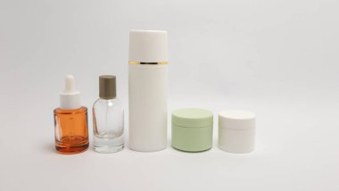 Serum şişeleri, sprey şişeleri ve krema kavanozları da dahil olmak üzere, temiz beyaz arka planda sıralanmış çeşitli kozmetik ürünlerinin stüdyo çekimi. Resim parlak bir şekilde ışıklandırılmış, ürünlerin ambalaj ve dokularını vurguluyor, ve bir va vurguluyor