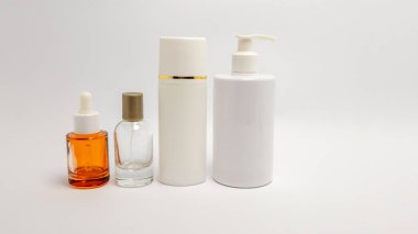 Bu resimde el değmemiş beyaz bir zemin üzerine yerleştirilmiş cilt bakımı ve güzellik ürünleri var. Kompozisyonda bir damlatıcı şişe, bir sprey şişesi, uzun bir silindirik şişe ve bir pompa şişesi de dahil olmak üzere farklı tipte şişeler yer alıyor.