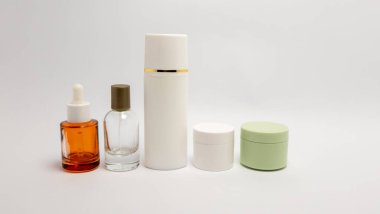 Bir stüdyo çekiminde, içinde damlalar ve sprey pompalar bulunan şişeler ve kremler için kavanozlar bulunan cilt bakım ürünleri sergileniyor. Eşyalar el değmemiş beyaz bir arkaplanda saf ve modern bir estetik oluşturacak şekilde sıralanmış. İma.