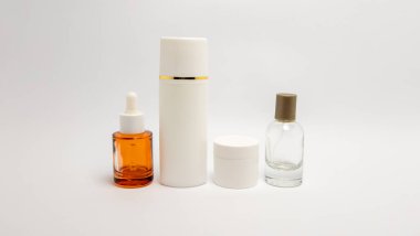 Düşürme şişesi, uzun şişe, küçük kavanoz ve arka planda beyaz bir arka planda dizilmiş bir sprey şişesi de dahil olmak üzere minimalist kozmetik şişelerden oluşan bir koleksiyon. Şişeler çeşitli şekil ve boyutlarda, temiz ve modern bir estetik sunuyor.,