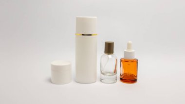 Bir stüdyo resmi, beyaz bir zemine karşı düzenlenmiş güzellik ürünleri koleksiyonunu sergiliyor. Görüntü bir kavanoz, uzun bir şişe, bir sprey şişesi ve bir damlatıcı şişeden oluşuyor. Estetik temiz ve minimalist, ürünlerin tasarımını vurguluyor.
