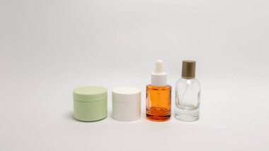 Temiz, beyaz bir zemine karşı peş peşe dizilmiş dört cilt ürününden oluşan bir koleksiyon. Sette kapaklı iki küçük kavanoz, bir damla şişesi ve bir sprey şişesi yer alıyor. Renkler yeşil, beyaz ve kehribar camların karışımı, modern ve mi