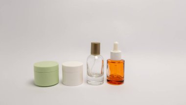 Temiz beyaz arka planda sergilenen bir cilt ürünleri koleksiyonu. Anlaşmada iki kavanoz ve biri turuncu sıvıyla dolu olan iki şişe yer alıyor. Kompozisyon minimalist, ürünlerin tasarımını vurguluyor.