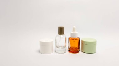 Düz beyaz bir zemine dizilmiş cilt ürünlerinin yer aldığı minimalist bir stüdyo çekimi. Resim, kavanozlar ve şişeler de dahil olmak üzere çeşitli kozmetik kaplar sergiliyor. Kompozisyon, temiz çizgileri ve modern estetiği vurguluyor. Ürün.