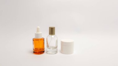 Üç kozmetik konteynır beyaz arka planda sergileniyor, bir cilt serumu şişesi, açık bir sprey şişesi ve beyaz bir kavanoz sergileniyor. Kompozisyon temiz ve minimalist, ürünleri vurguluyor. Tarafsız arka plan bir 