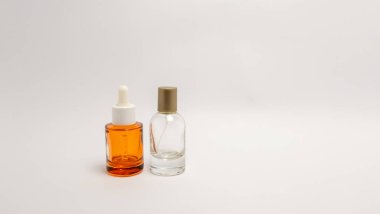 İki cilt bakımı şişesi geniş bir kopya alanına sahip düz beyaz bir arka planda sergilenir. Bir şişe turuncu bardakta, diğeri de sprey kapaklı cam. Işıklandırma yumuşak ve eşit, temiz, minimalist bir estetik oluşturuyor. Mükemmel.