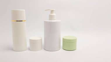 Güzellik ürünleri koleksiyonunun yer aldığı temiz, minimalist bir fotoğraf. Görüntü çeşitli kozmetik kapları gösteriyor. Uzun bir sprey şişesi, bir pompa şişesi ve iki küçük kavanoz da dahil. Kompozisyon basit, ürünler karşı düzenlenmiş.