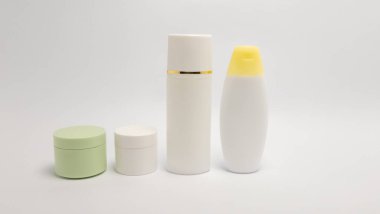 Beyaz bir yüzeye yerleştirilmiş çeşitli kozmetik ürün kapları. Görüntüde bir kavanoz, küçük bir kap, uzun bir pompa şişesi ve sarı başlıklı bir sıkma şişe yer alıyor. Ürünler temiz, beyaz bir arka tarafa yerleştirilmiş.