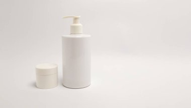 Basit bir stüdyo çekiminde beyaz bir arka planda iki beyaz kozmetik konteynır bulunur. Uzun bir pompa şişesi, her ikisi de minimalist estetik olan küçük bir kavanozun yanına yerleştirilir. Temiz ve parlak görüntü güzellik ve cilt ürünlerinin tanıtımı için idealdir. Ben...