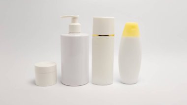 İçinde losyon makinesi, sprey şişesi ve kavanoz bulunan beyaz kozmetik şişeleri. Konteynırlar düz beyaz bir zemine göre düzenlenerek minimalist ve temiz bir estetik oluşturuyor. Ürün sunumları için mükemmel