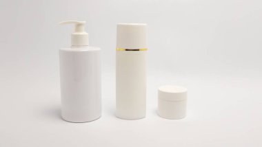 Beyaz arka planda üç kozmetik ürün konteynırı düzenleniyor. Kutular arasında bir pompa şişesi, altın bantlı uzun bir silindirik şişe ve kapaklı küçük bir kavanoz yer alıyor. Minimalist tasarım ve temiz estetik cilt bakımına odaklandığını gösteriyor. 