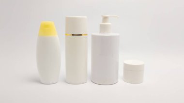 Beyaz tenli ürün şişeleri ve kavanozlarından oluşan bir koleksiyon düz beyaz bir arkaplana karşı sıraya dizilir. Görüntü çeşitli kozmetik kapları sergiliyor. Pompalı losyon şişesi, krem kavanozu ve şampuan şişesi de dahil. Minimalist.