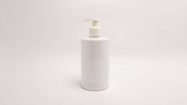 Pompalı beyaz plastik bir şişenin basit bir stüdyo resmi. Şişe sade beyaz bir arka planda duruyor, temiz ve minimalist bir estetik oluşturuyor. Resim parlak bir şekilde ışıklandırılmış, şişenin şeklini ve pompa mekanizmasını vurguluyor. Uygun olur.
