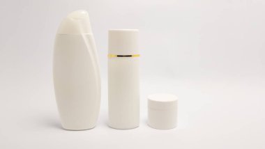 Uzun bir şampuan veya losyon şişesi, silindirik bir pompa şişesi ve küçük bir kavanoz dahil olmak üzere üç beyaz kozmetik şişenin yer aldığı bir stüdyo çekimi. Şişeler beyaz bir zemin üzerinde sade beyaz bir zemin üzerinde, temiz ve minimalis vurgulanıyor.