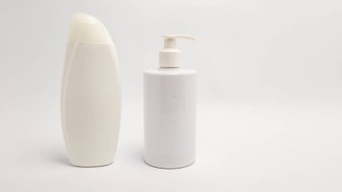 Beyaz arka planda iki beyaz kozmetik şişesinin yer aldığı bir stüdyo resmi. Bir şişe klasik oval şekilli ve kapaklı, diğerinde de pompa makinesi var. Görüntü temiz estetiği vurguluyor. Ürün sunumları için mükemmel.