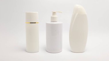 Beyaz arka planda üç farklı kozmetik ürün şişesinin yer aldığı bir stüdyo resmi. Şişeler arasında altın bantlı uzun silindirik bir kap, bir pompa şişesi ve oval şekilli yuvarlak bir şişe yer alıyor. Işıklar eşit ve...