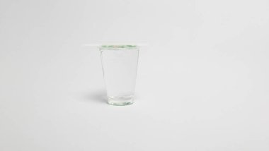 Temiz, beyaz bir zemin üzerine kurulmuş, üzerinde bir pipet olan tek bir bardak temiz su. Görüntü, suyun basitliğini ve saflığını vurguluyor ve canlandırıcı niteliklerini vurguluyor. Yumuşak ışıklandırmalı minimalist kompozisyon