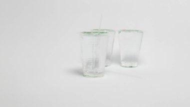 Stüdyo çekiminde, temiz beyaz bir arkaplan üzerine yerleştirilmiş pipetli üç cam bardak vardı. Bardaklar boş görünüyor, ışık yumuşak ve dağınık, minimalist ve nötr bir estetik oluşturuyor. Görüntü basitliğe odaklanır