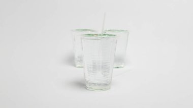 Bir stüdyo çekiminde suyla dolu üç temiz plastik bardak yer alır. Bir bardak ön planda, içine bir pipet yerleştirilmiş. Diğer iki fincan arka planda bulanık. Üç kupa da düz beyaz bir zeminde oturuyor. Kompozisyon temiz ve simülasyon