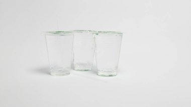 Üç şeffaf plastik bardak sıvı, muhtemelen su ile dolu, düz beyaz bir yüzey üzerinde düzenlenmiştir. Her fincanın bir kapağı ve pipeti var. Fotoğraf, yumuşak gölgelerle iyi aydınlatılmış ve objelerin basitliği ve berraklığına odaklanmış. İletişim.