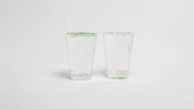 Bir stüdyo çekimi beyaz arka planda iki cam bardak sunar. Bir fincanın içine bir pipet yerleştirilirken, bir pipet de bardakların yanında duruyor. Kompozisyon basit, tarafsız bir zemin ile, fincanlara ve pipetlere odaklanmayı sağlıyor. Işıklar eşit.,