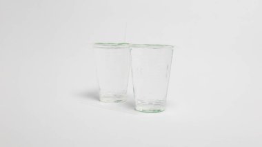 İki şeffaf, boş bardak beyaz bir yüzeye yerleştirilir. Bardakların yanına iki pipet konur ve bir pipet bardaklardan birine yerleştirilir. Görüntü sığ bir alan derinliği ile çekiliyor ve camlar camdan yapılmış gibi görünüyor. Şey... 