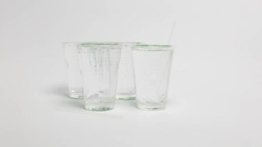 Beyaz arka planda suyla dolu dört cam bardağın yer aldığı minimalist bir stüdyo resmi. Bir bardağın içine bir pipet yerleştirilmiş. Görüntü, suyun berraklığını ve kompozisyonun basitliğini vurgular. Temiz ve ferahlatıcı bir aes oluşturur.