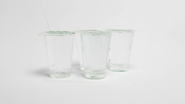 Bir stüdyo çekiminde her biri plastik kapakla mühürlenmiş, suyla dolu dört şeffaf plastik bardak yer alır. Çubuklar bardakların bazılarına yerleştiriliyor ve yüzeyde birkaç pipet var. Sahne, temiz beyaz bir arkaplana göre ayarlandı.