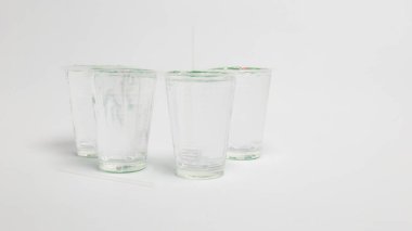 Önlerinde iki pipet bulunan beyaz bir yüzeye dizilmiş dört temiz, boş bardak. Bardaklar camdan yapılmış gibi görünüyor ve boş. Doldurulmaya hazır olduklarını gösteriyor. Temiz, minimalist ortam bir sadelik hissi yaratır.