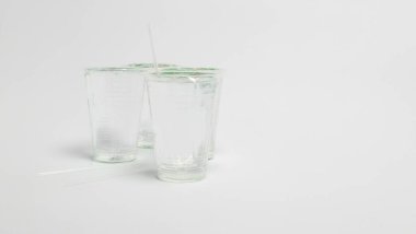 Bir natürmort, parlak beyaz bir yüzeye yerleştirilmiş üç temiz plastik bardak ve iki pipet sergiler. Bardaklar boş, etrafındaki ışığı yansıtıyor ve içlerinden birine tek bir pipet yerleştiriliyor. Resim basitliği ve döngüyü vurgular