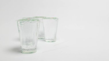 Üç berrak su bardağının yer aldığı bir stüdyo resmi, bazılarının kapağı ve iki pipet, hepsi de el değmemiş beyaz arka planda. Bardaklar boş, içecek bir şeyler ikram edeyim. Kompozisyon basit ve temiz. Suyun berraklığını vurguluyor.