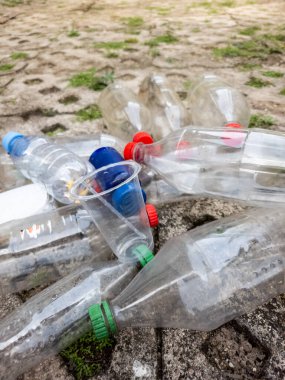 Çeşitli plastik şişelerin yakın çekimi ve desenli bir zemin yüzeyine atılmış bir fincan. Görüntü, plastik kirliliği ve çevre üzerindeki etkisini vurguluyor. Kompozisyonda farklı tipte plastik kaplar gösteriliyor.