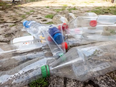 Yakın planda atılan plastik şişeler ve dışarıda beton bir yüzey üzerinde duran plastik bardaklar görülüyor. Şişeler boş ve çeşitli boyutlarda. Bu resim çevre kirliliği, geri dönüşüm sorunları ve sorumlu atık ihtiyacını vurgular
