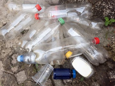 Bu resim, beton bir yüzeye saçılmış atılmış plastik şişeler ve diğer çöpleri gösteriyor. Kompozisyonda plastik kirliliği sorunu ve bunun çevresel etkisi vurgulanıyor. Fotoğrafta çeşitli plastik bulaşıcı maddeler var.