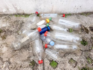 Çöpe atılmış plastik şişeler ve bir fincan, beton bir yüzeye saçılmıştır. Görüntü, çevre kirliliği, atık ve insan faaliyetlerinin etkilerini aktarıyor. Kompozisyon, plastik atık ve pres sorununu vurguluyor