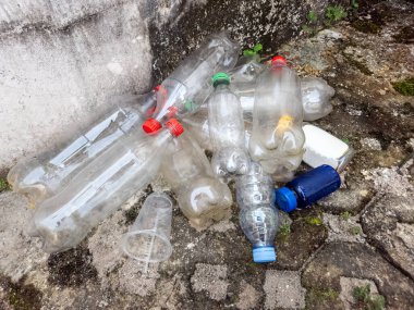 Dökümlü bir yüzeye saçılmış plastik şişe ve konteynır koleksiyonu. Görüntü çevresel kirliliği ve atıkların etkisini vurguluyor. Kompozisyon, plastik sorununu vurgulayan çeşitli şekil ve renklere sahiptir.