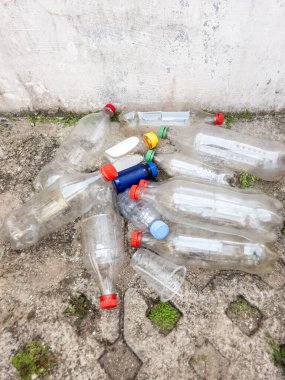Plastik atıkların çevresel etkilerini betimleyen, beton bir yüzeye saçılmış bir plastik şişe ve bir kupa koleksiyonu. Görüntü kirlilik sorununu vurguluyor, geri dönüşüm ve atık yönetimi çözümlerine duyulan ihtiyacı vurguluyor. 