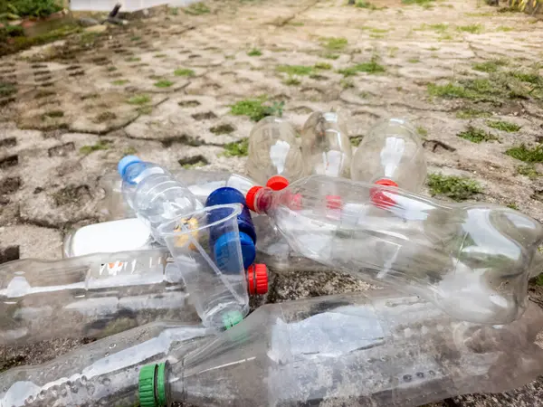 Yakın çekim, beton bir yüzeye saçılmış plastik şişe, bardak ve konteynırları gösteriyor. Görüntü, plastik atık, çevre kirliliği ve geri dönüşüm ve atık yönetimi ihtiyacını vurguluyor. Sahne aktarır