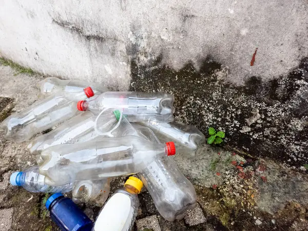 Kirli beton bir yüzey üzerinde atılmış plastik şişeler ve bir kupa koleksiyonu var. Görüntü, çevre kirliliği ve atık yönetimi sorunlarını gösteriyor. Şişeler çeşitli boyut ve renklerde, görünür aşınma ve yırtılmayla birlikte. Küçük bir plan.