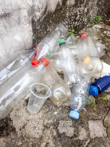 Yüksek açılı çekimde, atılmış plastik şişeler ve desenli bir zemin yüzeyine rastgele serpiştirilmiş bir fincan görülüyor. Sahne, özellikle temiz, mavi ve re de dahil olmak üzere plastik atık birikimi, çevre kirliliğini vurguluyor