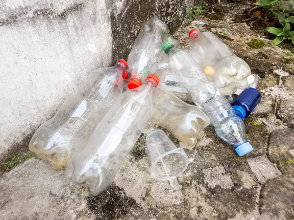 Çöpe atılmış plastik şişeler ve beton bir yüzeyde duran bir kupa. Görüntü kirlilik sorununu ve plastik atıkların çevresel etkilerini vurguluyor. Kompozisyonda plastik kapların çeşitli boyutları ve renkleri gösteriliyor.