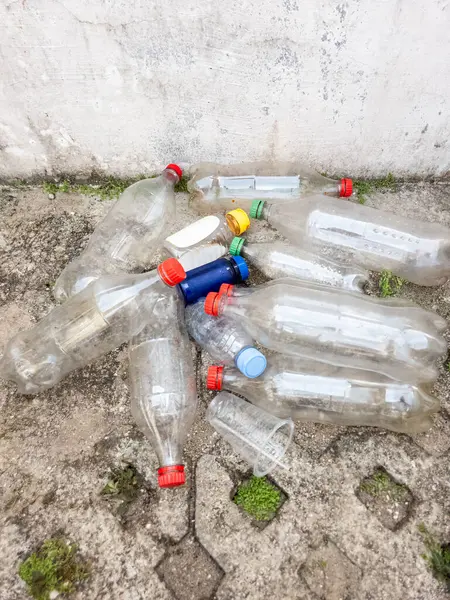 Plastik atıkların çevresel etkilerini betimleyen, beton bir yüzeye saçılmış bir plastik şişe ve bir kupa koleksiyonu. Görüntü kirlilik sorununu vurguluyor, geri dönüşüm ve atık yönetimi çözümlerine duyulan ihtiyacı vurguluyor. 
